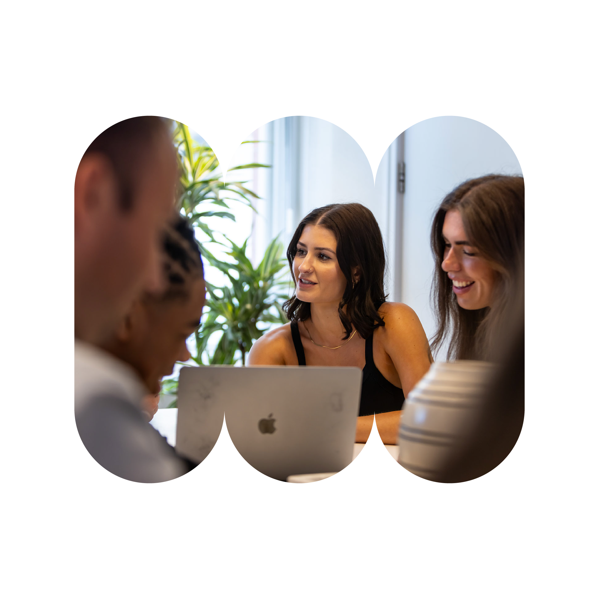 A woman is seated behind a laptop in conversation with colleagues who are out of frame