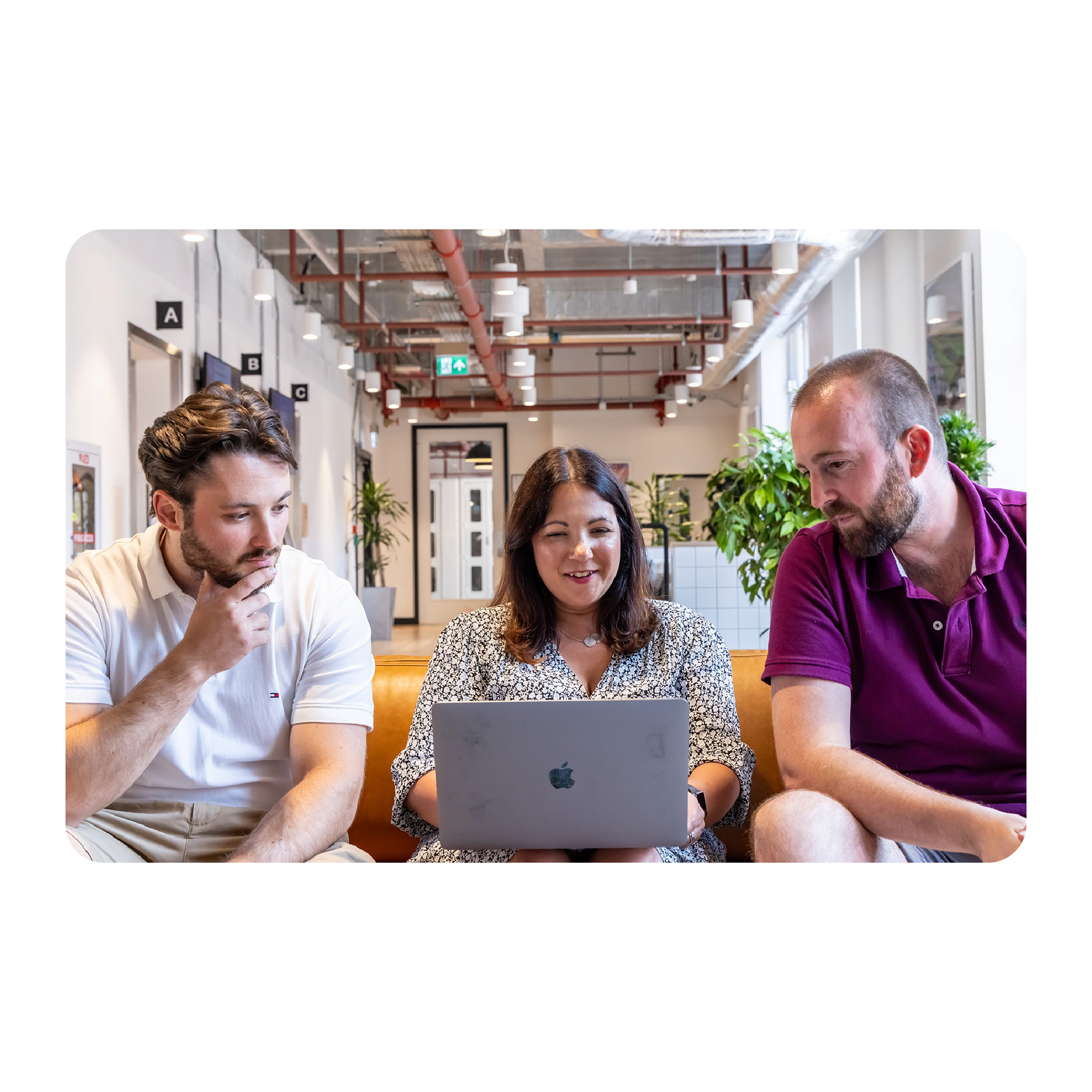 Two men and a woman are seated on a brown sofa looking at a laptop