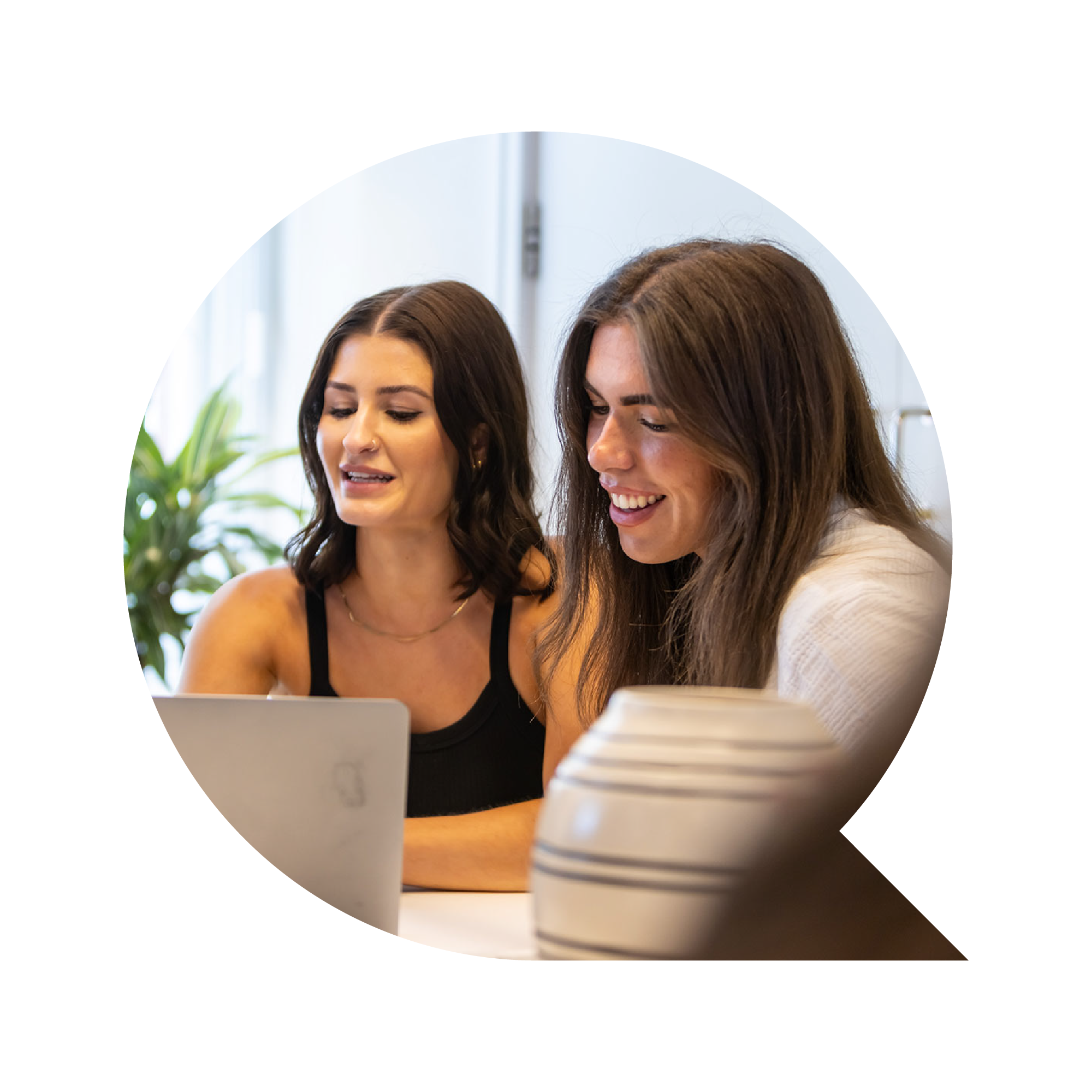 Two women are partnering on a project, using a laptop on the table in front of them