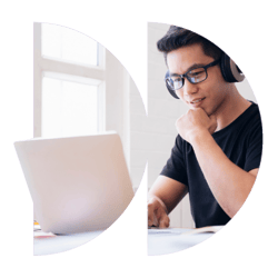 A man wearing headphones is sitting at a desk studying on a laptop