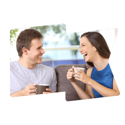 A man and a woman sit on a sofa laughing with cups of coffee in their hands