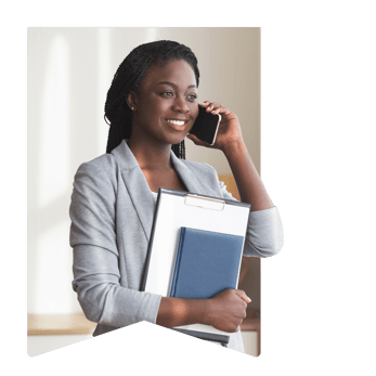 Woman is standing with a notebook tucked under her arm and speaking on the phone