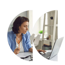 A lady sitting at her desk is holding a pencil and staring intently at her laptop