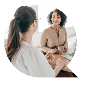 A female employee with her back to the camera is in discussion with another female employee