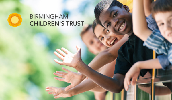 Four children are leaning over a railing in the right side of the frame waving towards the camera. In the left of the frame is the Birmingham Children's Trust text logo.