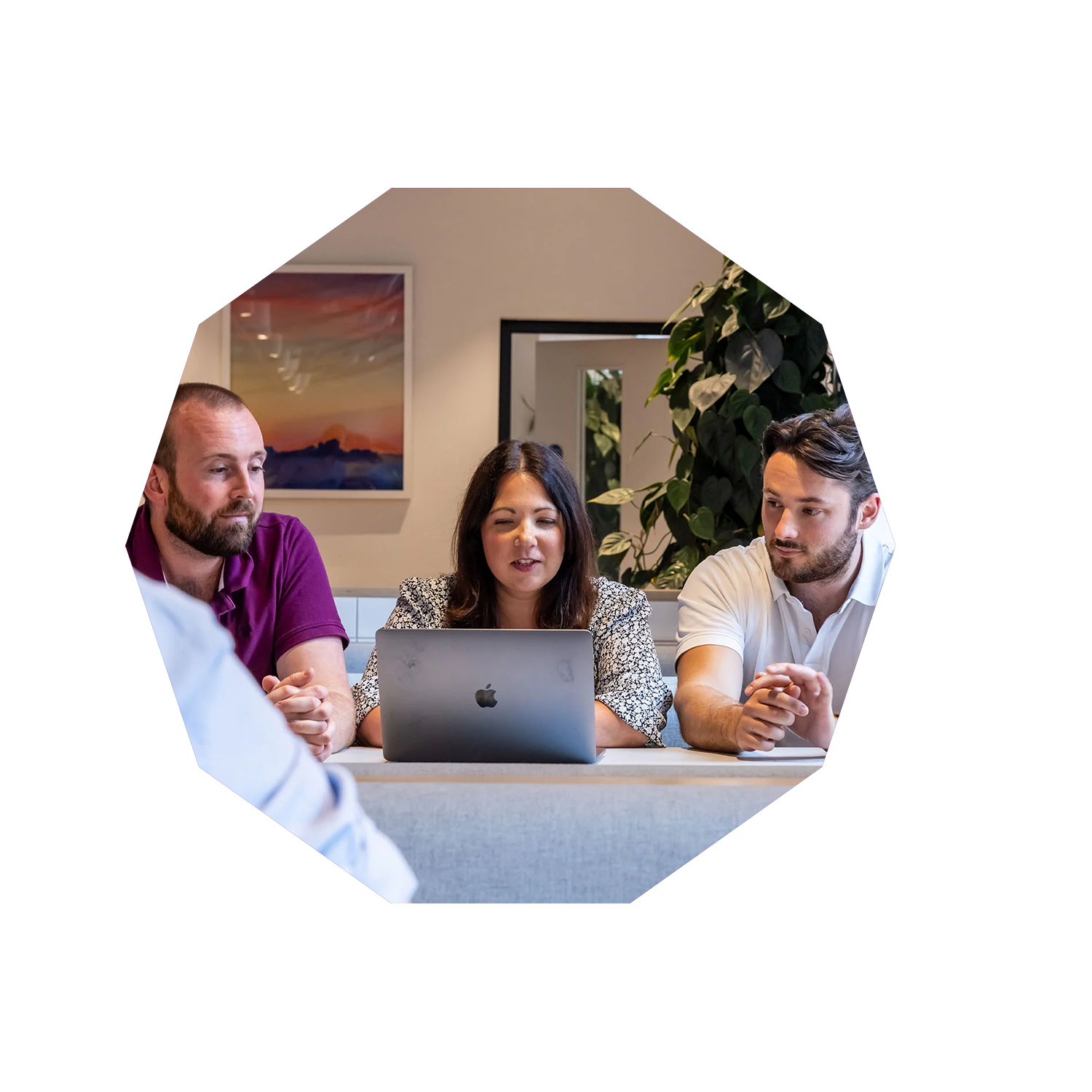 2 men and a woman are sat at a table looking at a laptop in the middle