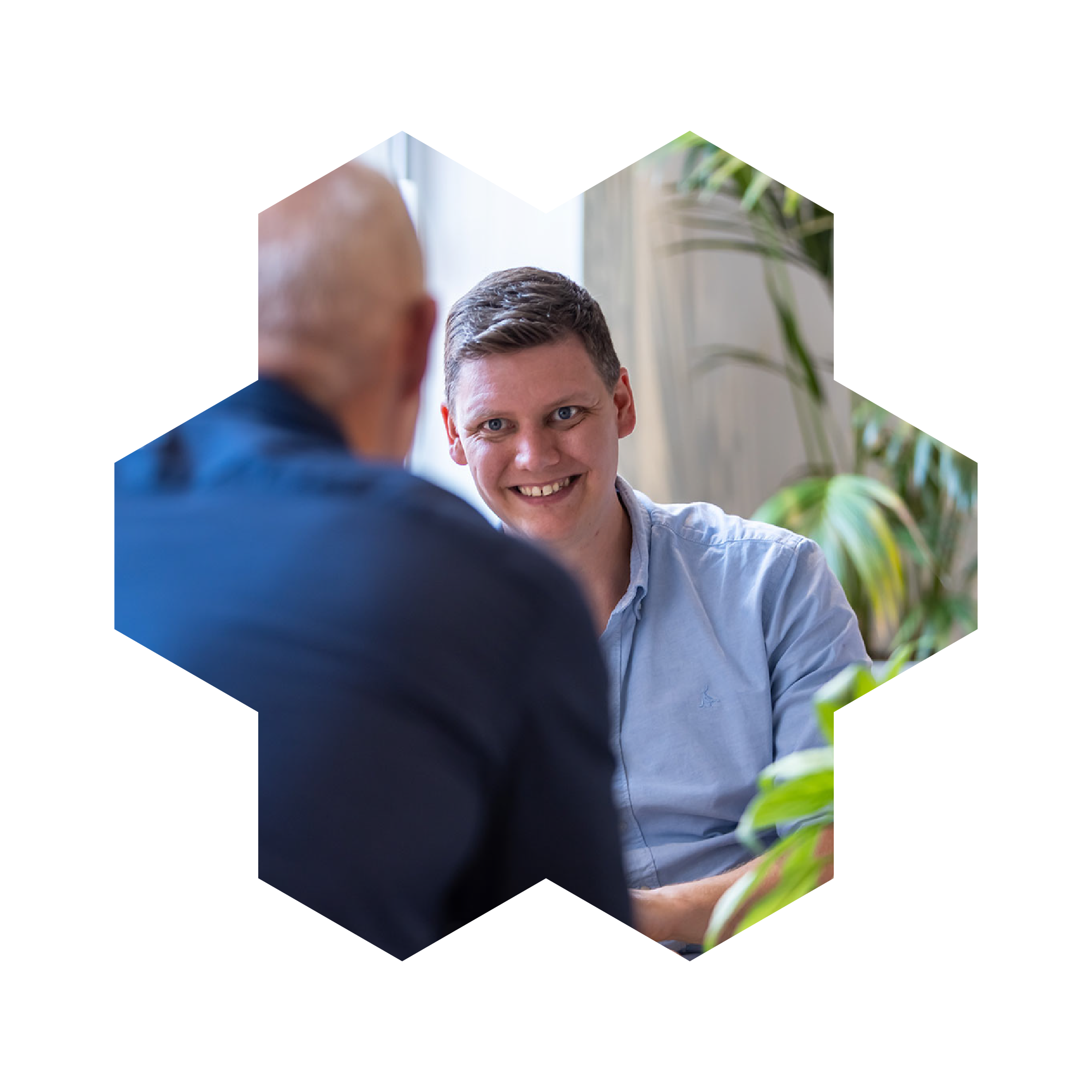 Man is smiling at a male colleague opposite him, whose back is to the camera