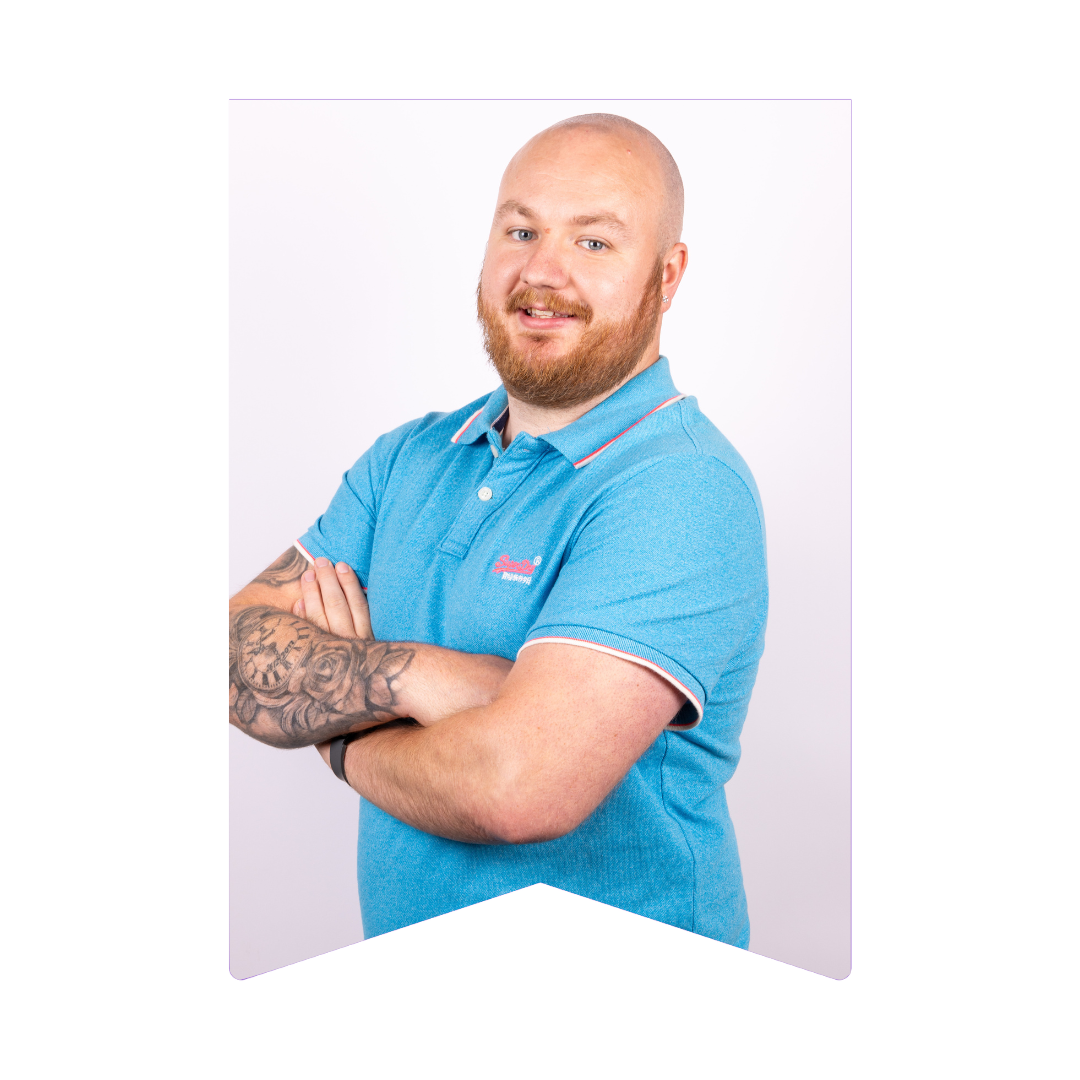 Daniel Flynn is wearing a light blue polo shirt and standing against a white backdrop with his arms crossed