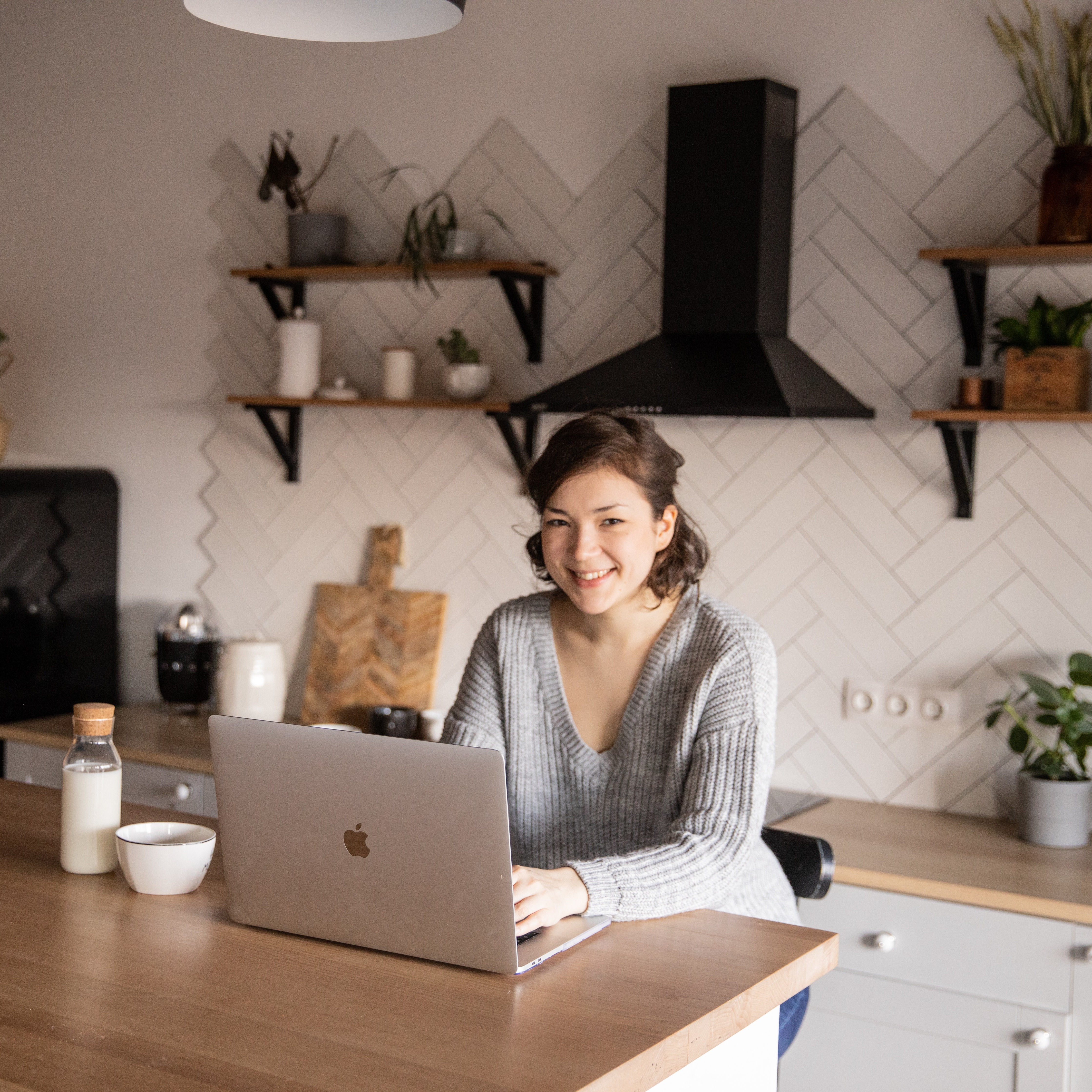 Lady in a grey jumper sitting at her kitchen counter typing on a laptop